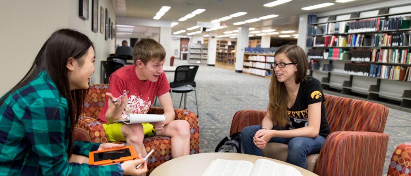 Three students talking at a table in the Main Library