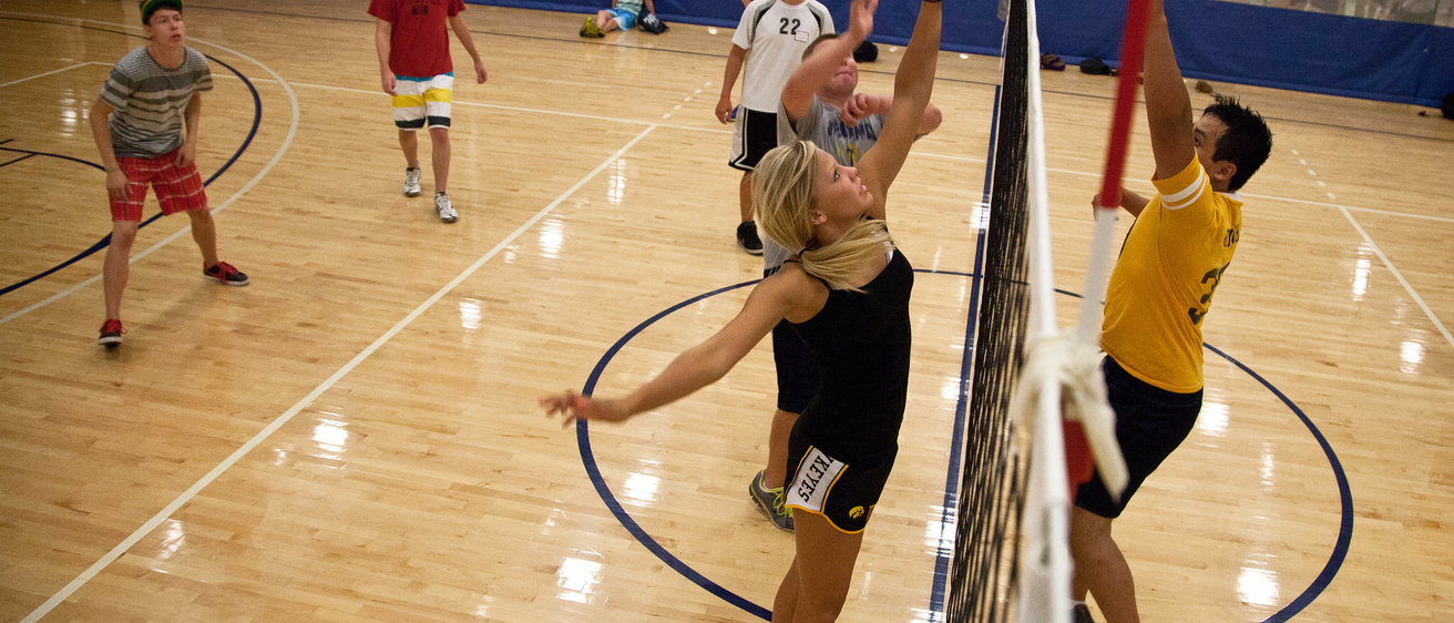 People jumping and hitting a volleyball in front of a net in a gym
