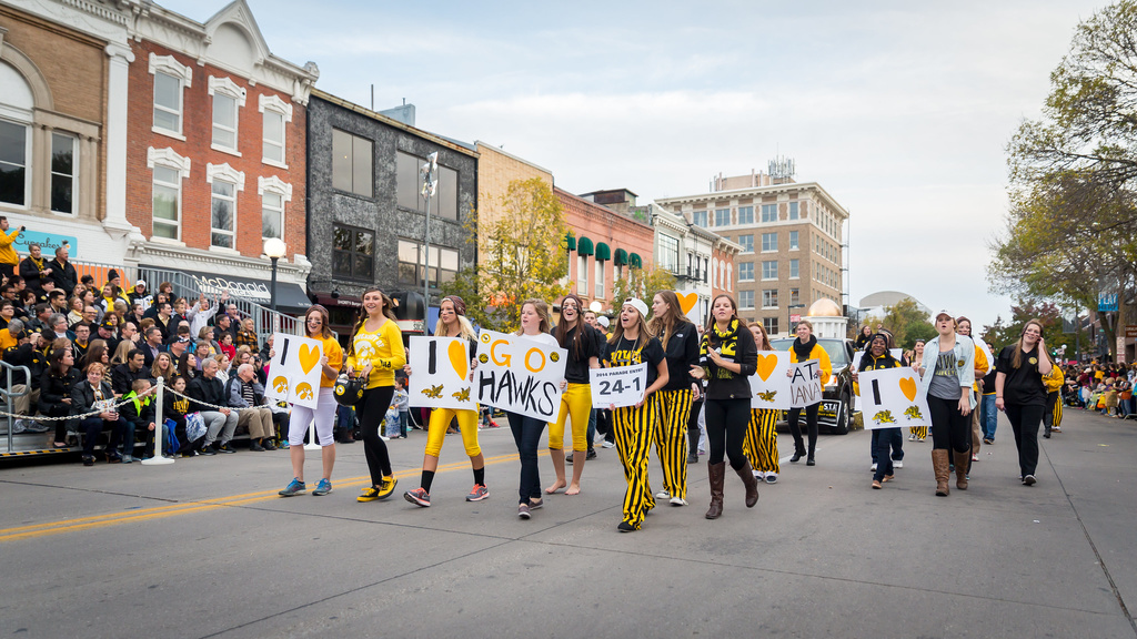 People walking in street during the homecoming parade with a sign that reads "Go Hawks!"