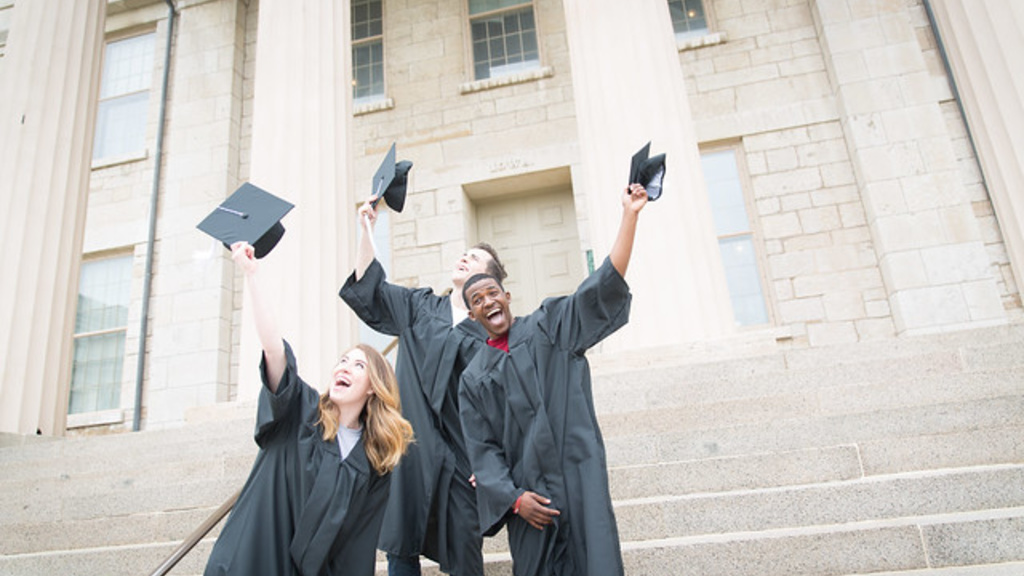 Three grads preparing to throw their graduation caps in front of the old capitol
