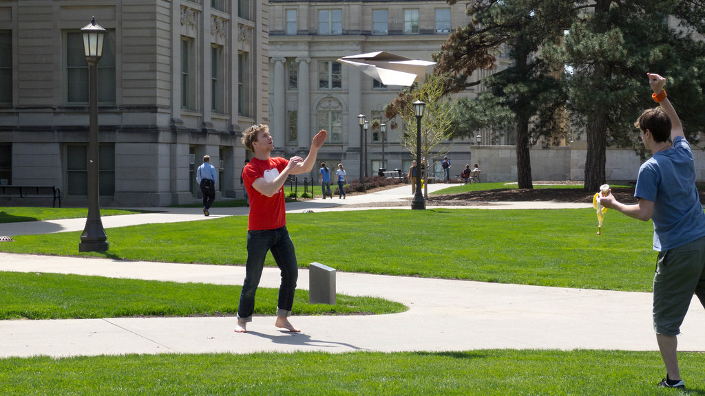 Student throwing a large paper airplane on the Pentacrest