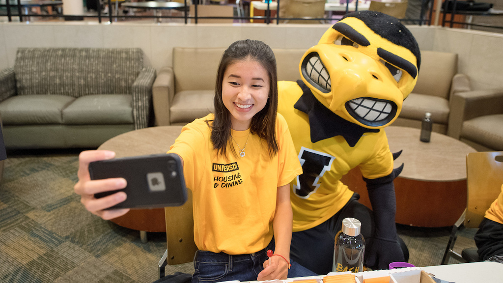 A person wearing a University Housing and Dining shirt taking a selfie with Herky